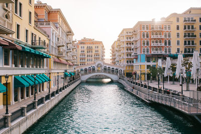 Colorful ornamental houses and canal with rippling water and bridge located against sunrise sky in morning on street of doha, qatar