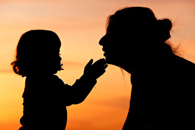 Silhouette of girl playing with mother against sky during sunset