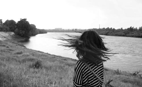 Rear view of woman with tossing hair on grassy field by river