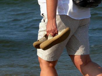 Low section of man holding umbrella against sea