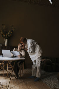 Non-binary person showing bills to friend while doing finance at home