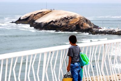 Rear view of boy standing at beach against sky