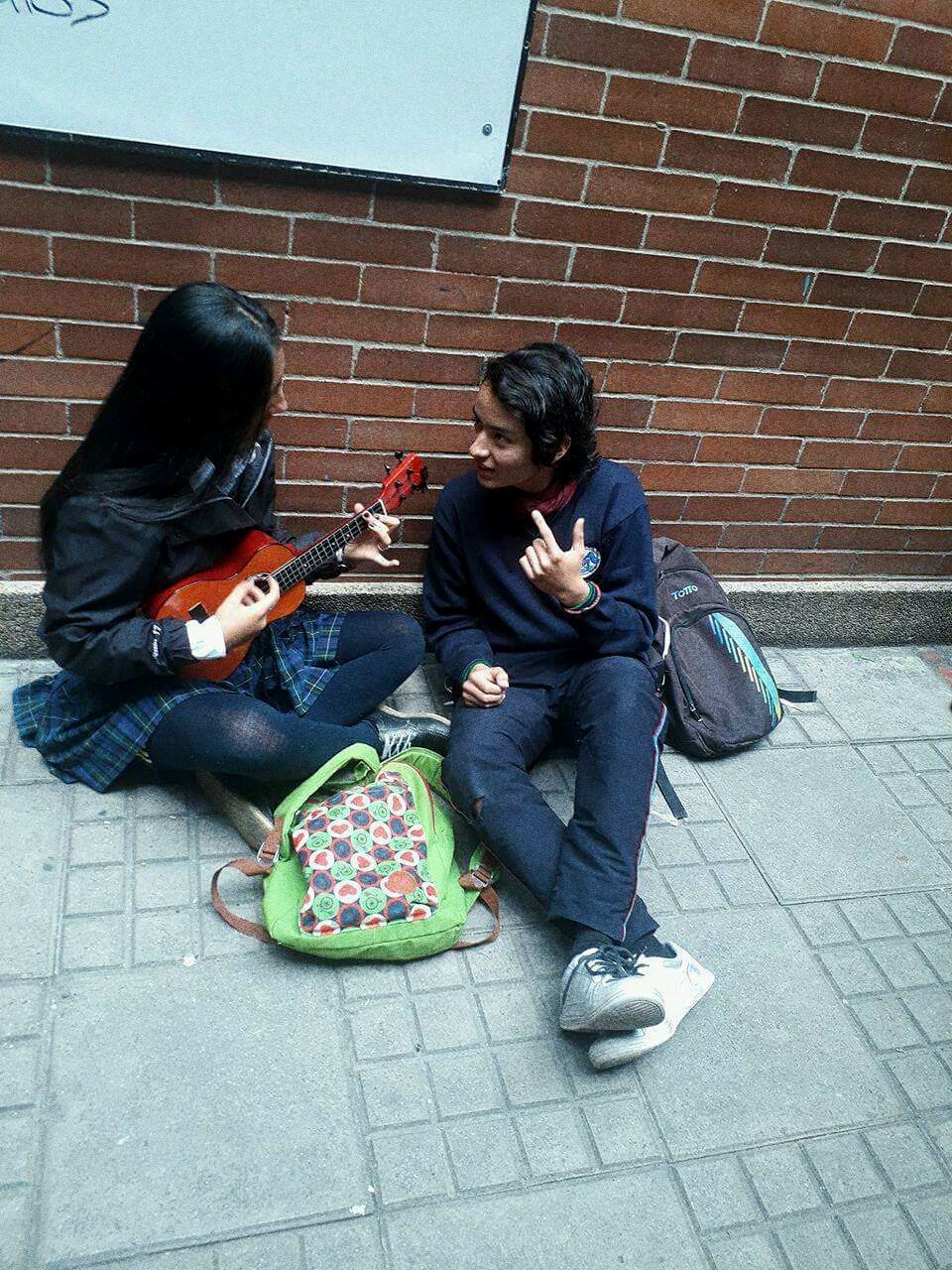 two people, brick wall, sitting, outdoors, togetherness, casual clothing, real people, full length, day, women, building exterior, built structure, men, friendship, city, musical instrument, guitar, young adult, architecture, young women, adult, people, adults only