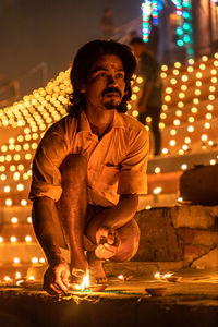 Full length of man sitting on illuminated fire at night