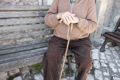 Midsection of man sitting on wooden bench