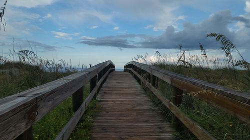 Wooden footbridge on land against sky