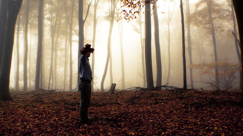 Side view of man holding bunch of autumn leaves in front of face in forest during foggy weather