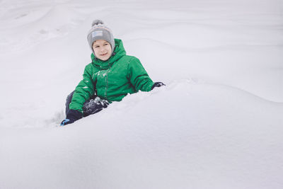 Happy boy sitting on snow in winter park. winter fun in the snow park.