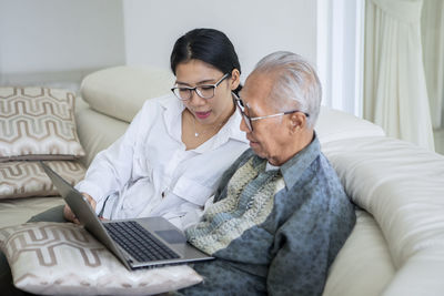 Grandchild teaching grandfather to use laptop at home 