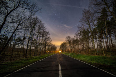 Diminishing road amidst trees at dusk