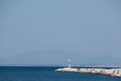 Lighthouse by sea against clear sky