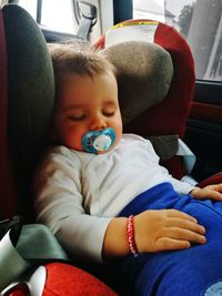 Cute baby boy sucking pacifier while sleeping in car