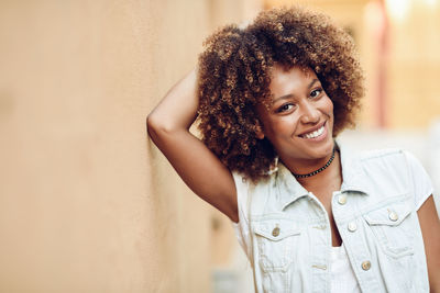 Portrait of smiling young woman with frizzy hair standing against wall