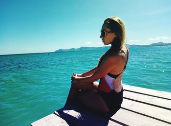 Side view of young woman sitting on pier over turquoise sea