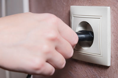 A female hand inserts an electric plug into a euro-format socket close-up