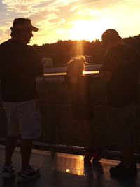 Rear view of people standing against sky during sunset