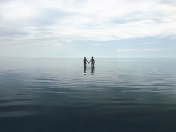 Siblings wading in sea against sky