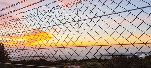 Chainlink fence on field against sky during sunset