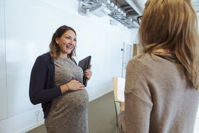 Smiling pregnant businesswoman discussing with colleague in board room