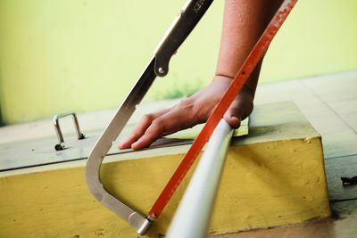 Cropped hands of man cutting pipe with hand saw