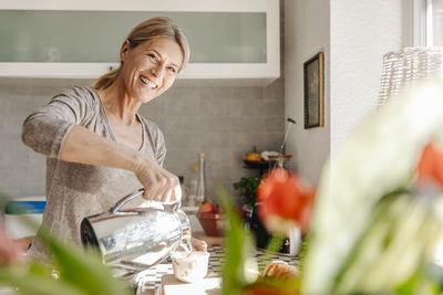 Happy woman at home in kitchen pouring coffee into cup