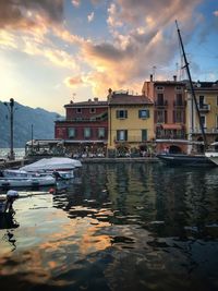 Sailboats moored on harbor by buildings against sky during sunset