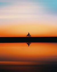 Silhouette person in sea against sky during sunset