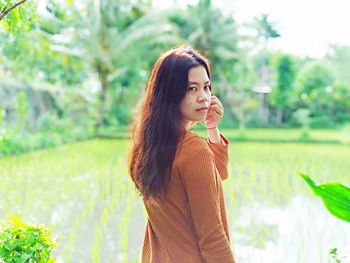 Young woman looking away while standing against plants