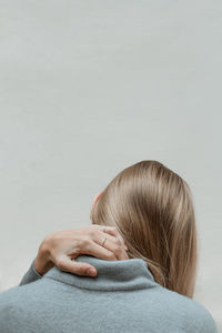 Rear view of woman holding neck against wall