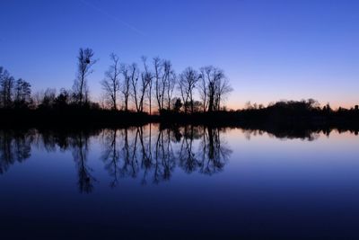 Reflection of silhouette trees in lake against blue sky