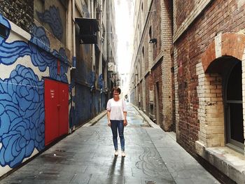 Full length of woman standing on alley amidst buildings in city