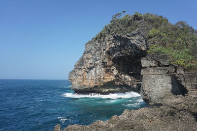 Rock formations in sea against clear blue sky