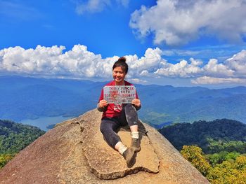 Portrait of man sitting on mountain against sky