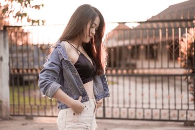 Seductive woman wearing denim jacket standing in city during sunset