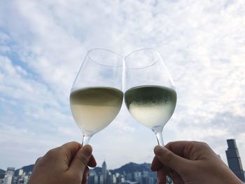 Close-up of hand holding wine glass against sky
