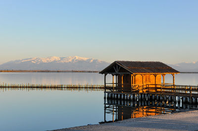 Built structure by lake against clear sky during sunset