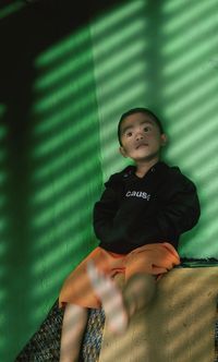 Boy looking away while sitting against wall at home