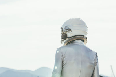 Back view man in spacesuit and helmet looking away while standing on path on sunny day in nature