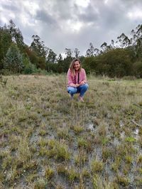 Full length of woman crouching on grass against sky