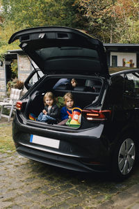 Sisters sitting in electric car trunk parked outside house