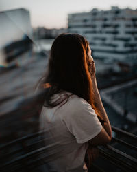 Rear view of woman standing in a balcony agaisnt urban city 