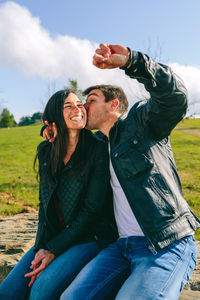 Happy couple kissing while taking a selfie with a smartwatch outdoors