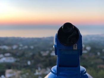 Close-up of coin-operated binoculars against cityscape during sunset