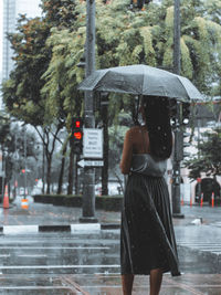 Rear view of woman standing on wet street in rain