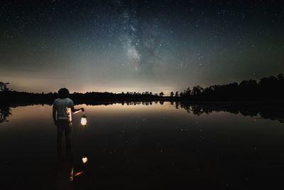 Man holding illuminated lantern while standing against lake at night