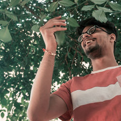 Portrait of young man with eyeglasses on plant against trees