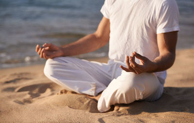 Midsection of man sitting on sand at beach