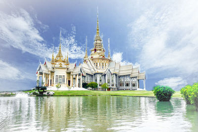 Temple building by lake against cloudy sky