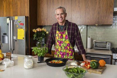 Portrait of smiling mature man preparing pizza in kitchen at home