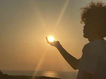 Side view of woman holding sparkler at sunset